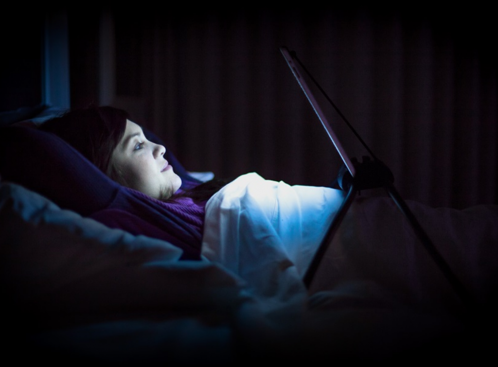 Mujer recostada sobre la cama mientras disfruta de contenido en su tablet sostenida en un soporte para cama