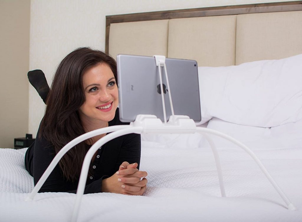 Mujer sonriendo mientras ve su tablet sostenida por soporte para camas