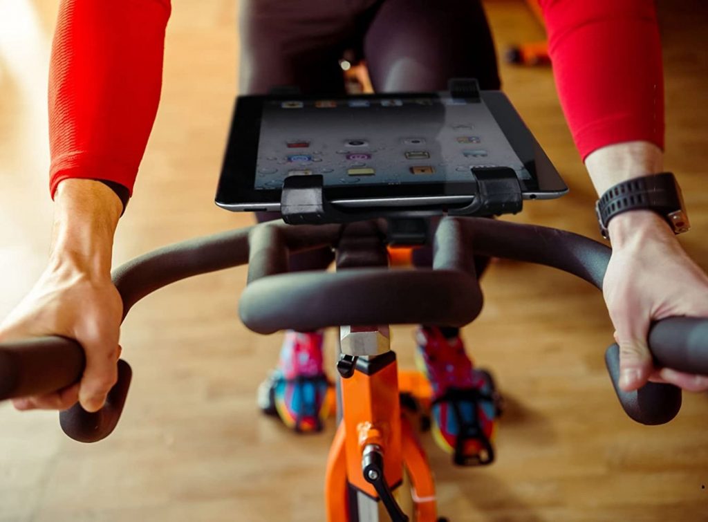 Persona ejercitándose en bicicleta estática con tablet suspendida por sujetador unido a la bicicleta