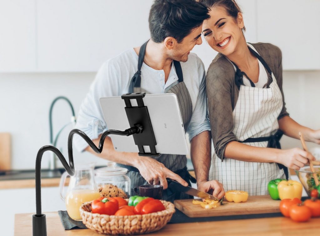 Pareja cocinando feliz mientras lee la receta en su tablet suspendida por un soporte de cuello de cisne
