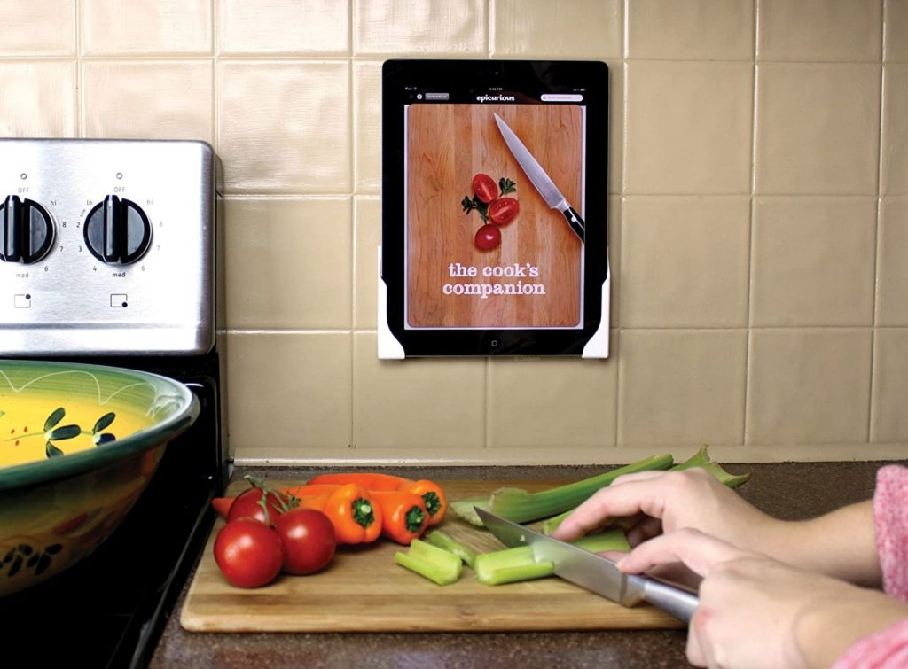 Mujer cocinando mientras observa la receta en una tablet sobre soporte en la pared