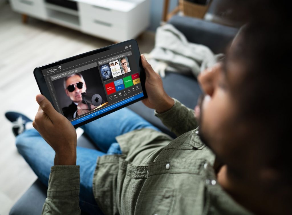 Hombre recostado en su sofá mientras ve películas en su tablet
